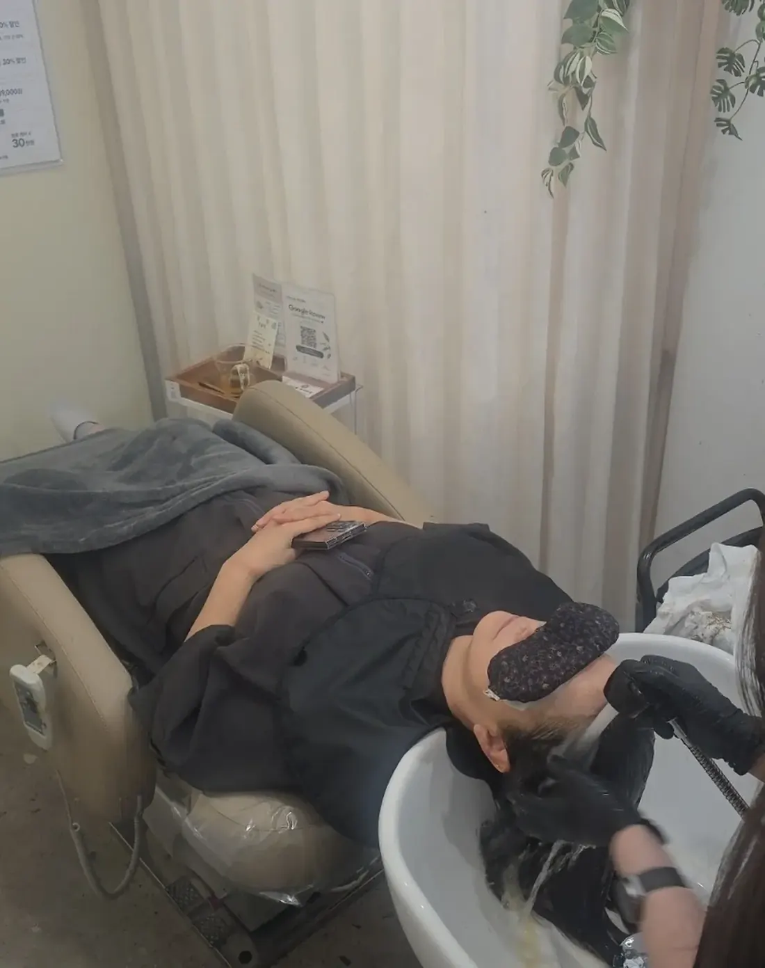 식물과 커튼이 보이는 공간에서 샴푸대에 누워 관리를 받는 고객