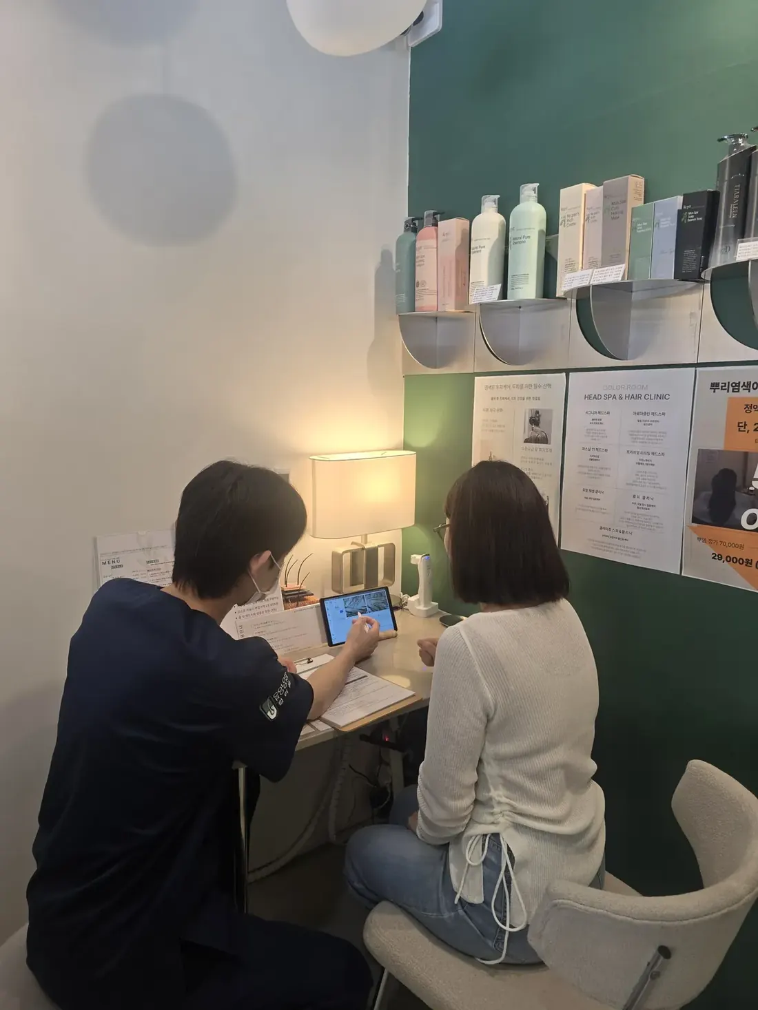 태블릿을 보며 상담하는 관리 담당자와 고객, 뒤편에 컬러룸 제품 선반